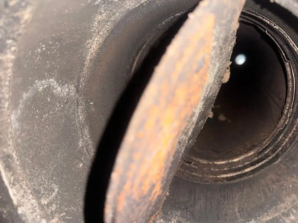 Inside a round metal flue, a rusted damper plate in the foreground and a small point of daylight far up the pipe.